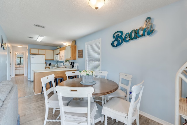 dining space with light hardwood / wood-style floors and a textured ceiling