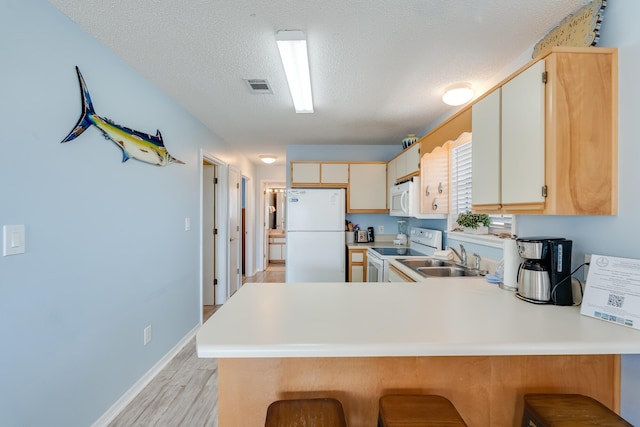 kitchen featuring kitchen peninsula, a textured ceiling, light hardwood / wood-style flooring, sink, and white appliances