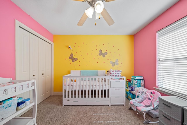 carpeted bedroom with a crib, a closet, and ceiling fan