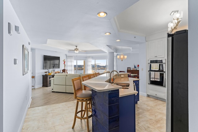 kitchen with a center island with sink, a raised ceiling, white cabinetry, a barn door, and sink