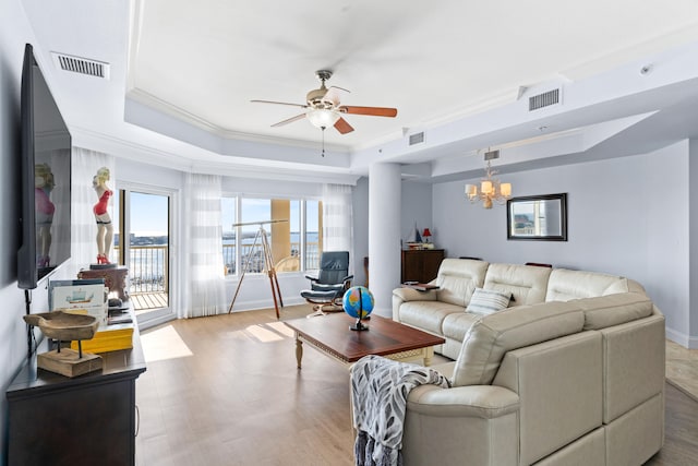 living room with crown molding, a raised ceiling, light hardwood / wood-style floors, and ceiling fan with notable chandelier