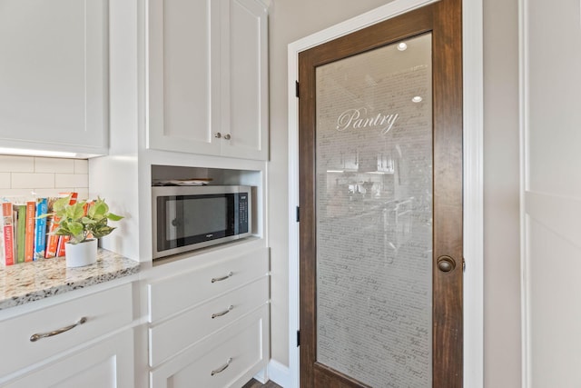 kitchen with decorative backsplash, white cabinetry, and light stone counters