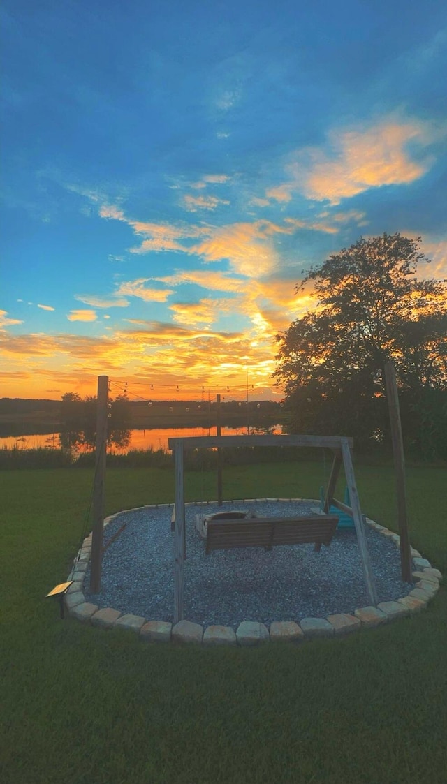 pool at dusk featuring a lawn and a water view