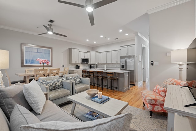 living room with ornamental molding, sink, light hardwood / wood-style floors, and ceiling fan