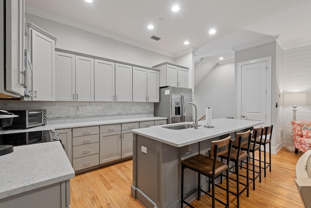 kitchen featuring stainless steel fridge, an island with sink, light hardwood / wood-style flooring, crown molding, and sink