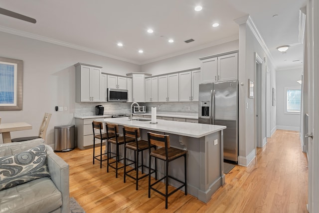 kitchen with decorative backsplash, light hardwood / wood-style flooring, stainless steel appliances, ornamental molding, and a breakfast bar