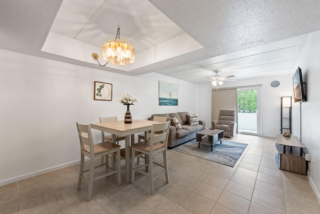 dining area with a tray ceiling, a textured ceiling, light tile patterned floors, and ceiling fan with notable chandelier