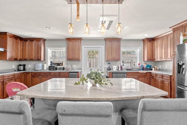 kitchen featuring a center island, stainless steel appliances, light stone counters, pendant lighting, and a breakfast bar area