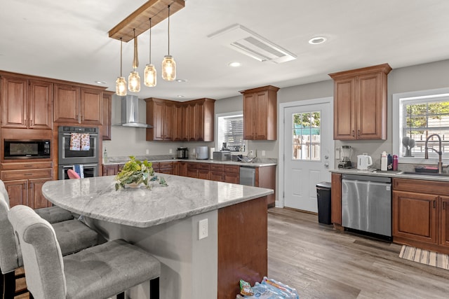 kitchen with a center island, wall chimney range hood, light hardwood / wood-style floors, light stone counters, and stainless steel appliances