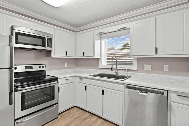 kitchen featuring appliances with stainless steel finishes, ornamental molding, a textured ceiling, sink, and white cabinetry