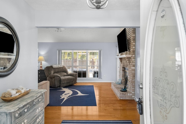 living room featuring a textured ceiling, light wood-type flooring, and a brick fireplace