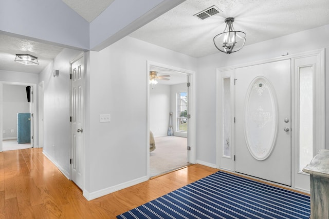 foyer entrance featuring wood-type flooring, a textured ceiling, and ceiling fan with notable chandelier