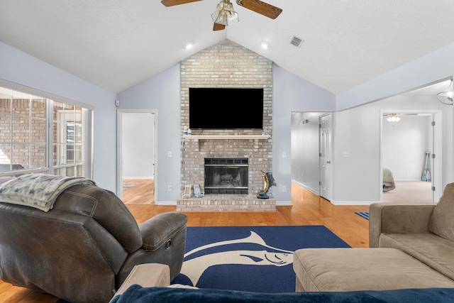 living room featuring vaulted ceiling, light hardwood / wood-style flooring, a brick fireplace, and ceiling fan