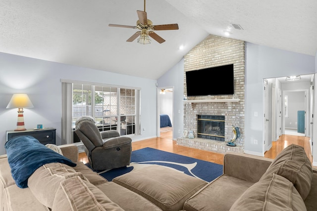 living room featuring light wood-type flooring, a textured ceiling, a brick fireplace, ceiling fan, and lofted ceiling