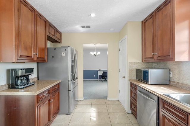 kitchen featuring stainless steel appliances, light tile patterned flooring, a notable chandelier, decorative light fixtures, and a textured ceiling