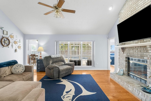 living room with ceiling fan, hardwood / wood-style flooring, lofted ceiling, and a brick fireplace