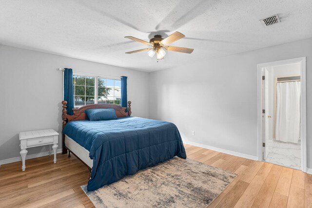 bedroom with ensuite bathroom, a textured ceiling, light wood-type flooring, and ceiling fan