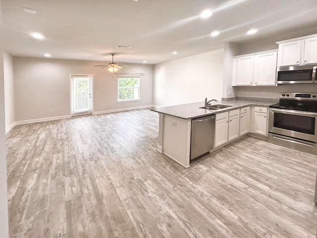 kitchen with kitchen peninsula, white cabinets, light wood-type flooring, sink, and stainless steel appliances