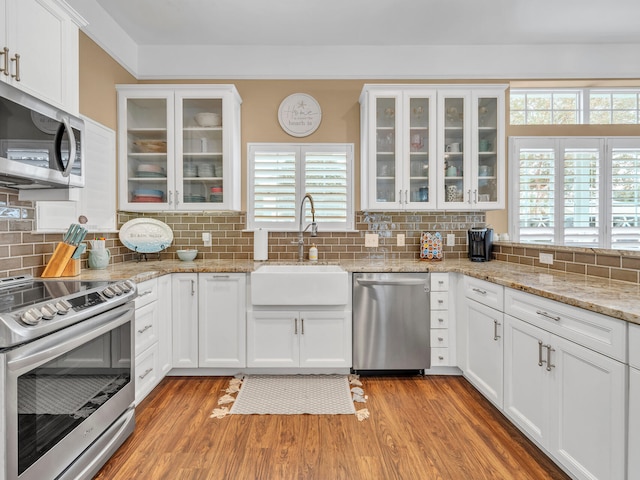 kitchen featuring sink, backsplash, light hardwood / wood-style floors, white cabinets, and appliances with stainless steel finishes