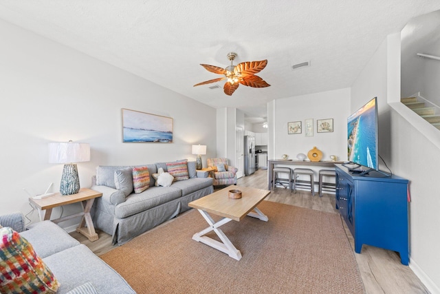 living room with light hardwood / wood-style floors, a textured ceiling, and ceiling fan