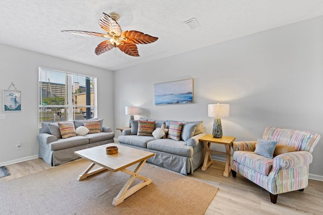 living room featuring ceiling fan, a textured ceiling, and light wood-type flooring