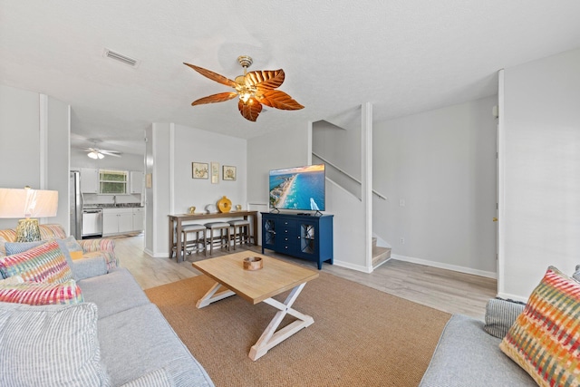 living room featuring ceiling fan, a textured ceiling, sink, and light wood-type flooring