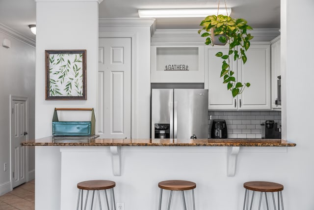 kitchen with white cabinets, a kitchen breakfast bar, kitchen peninsula, dark stone countertops, and stainless steel fridge with ice dispenser