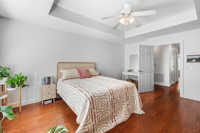 bedroom with dark hardwood / wood-style floors, a raised ceiling, and ceiling fan