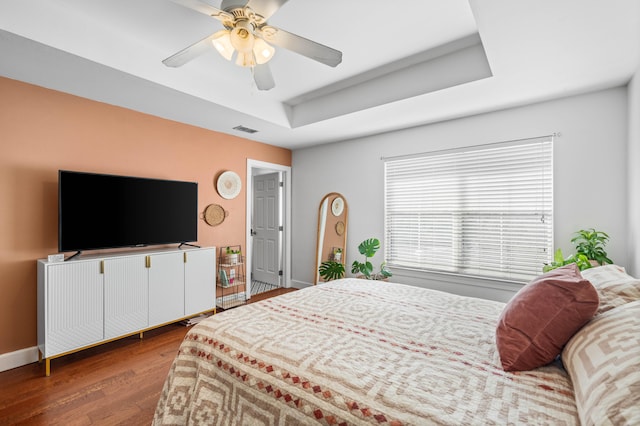 bedroom with a raised ceiling, ceiling fan, and dark wood-type flooring