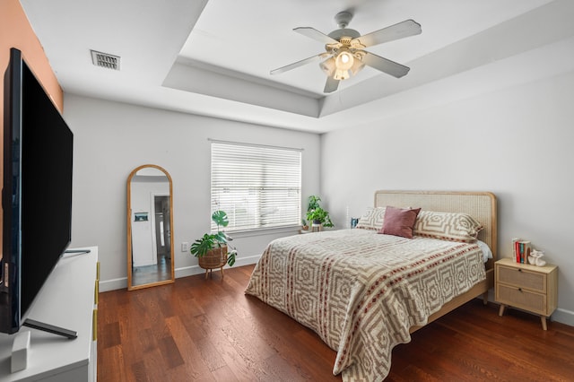 bedroom featuring ceiling fan, dark hardwood / wood-style floors, and a tray ceiling