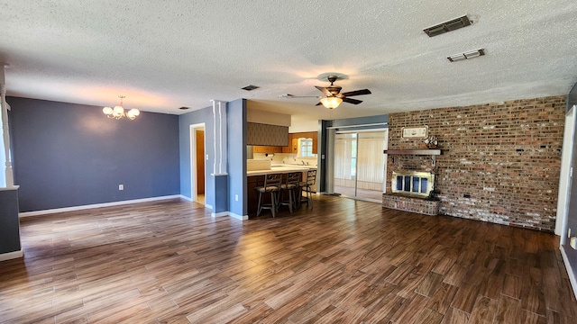 unfurnished living room with ceiling fan with notable chandelier, a textured ceiling, a brick fireplace, and dark hardwood / wood-style floors