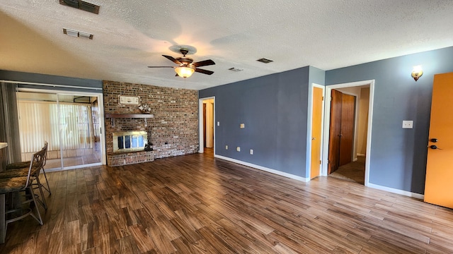 unfurnished living room with ceiling fan, a textured ceiling, wood-type flooring, and a brick fireplace