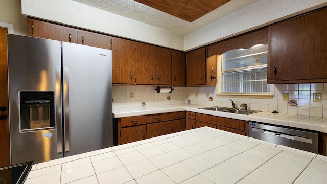 kitchen with decorative backsplash, appliances with stainless steel finishes, a textured ceiling, tile counters, and sink