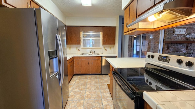 kitchen with appliances with stainless steel finishes, sink, light tile patterned flooring, a textured ceiling, and decorative backsplash