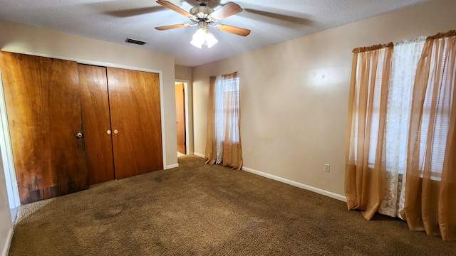 unfurnished bedroom with dark carpet, a textured ceiling, a closet, and ceiling fan