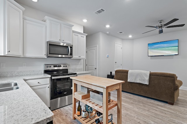 kitchen featuring ceiling fan, stainless steel appliances, light stone counters, light hardwood / wood-style floors, and white cabinets