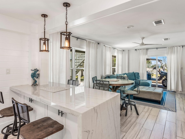 kitchen featuring kitchen peninsula, a kitchen bar, pendant lighting, light stone counters, and light hardwood / wood-style floors