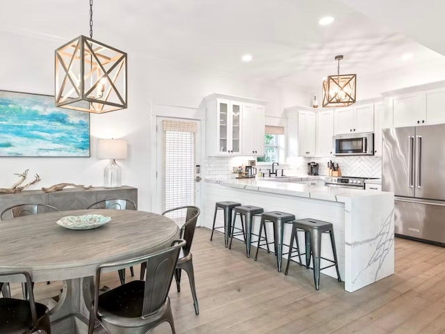 kitchen featuring stainless steel appliances, light hardwood / wood-style flooring, pendant lighting, and white cabinets