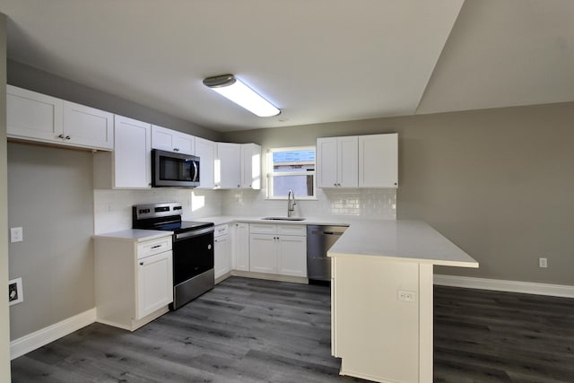 kitchen with appliances with stainless steel finishes, white cabinetry, sink, dark hardwood / wood-style flooring, and kitchen peninsula