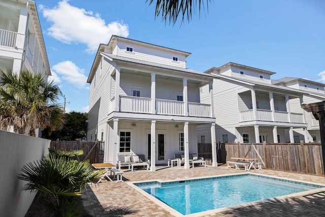 back of property featuring a balcony, a patio, and a fenced in pool