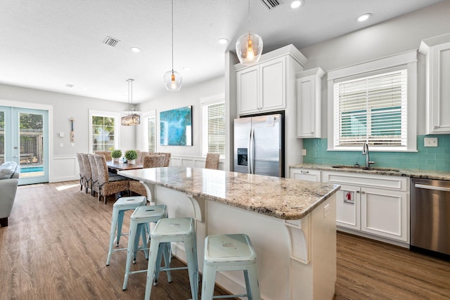 kitchen with stainless steel appliances, a center island, decorative light fixtures, and white cabinets