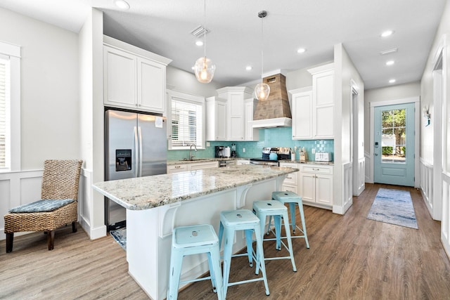 kitchen featuring a kitchen island, stainless steel appliances, pendant lighting, custom exhaust hood, and white cabinetry