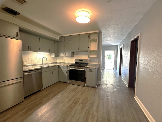 kitchen with decorative backsplash, sink, stainless steel appliances, and light hardwood / wood-style flooring