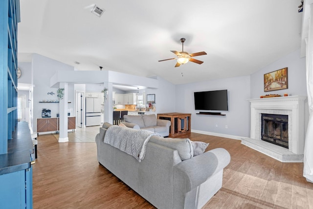 living room featuring light hardwood / wood-style flooring, ceiling fan, a fireplace, and vaulted ceiling