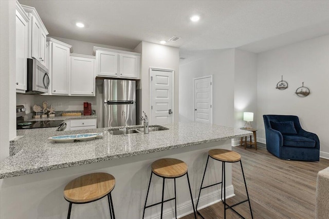 kitchen featuring white cabinetry, appliances with stainless steel finishes, wood-type flooring, and light stone countertops