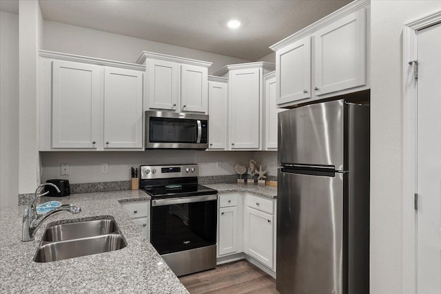 kitchen with stainless steel appliances, white cabinets, sink, and light stone counters