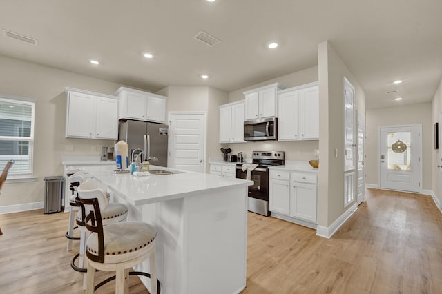 kitchen with a wealth of natural light, white cabinetry, a kitchen island with sink, and appliances with stainless steel finishes