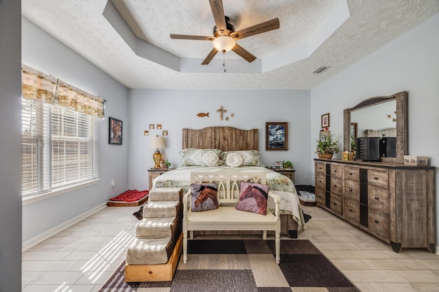 bedroom with a textured ceiling, light tile patterned floors, a tray ceiling, and ceiling fan