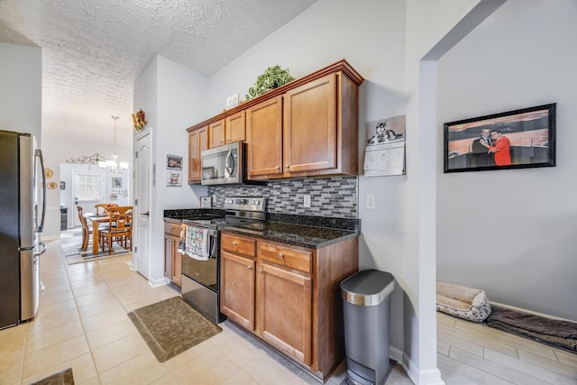 kitchen featuring tasteful backsplash, a textured ceiling, stainless steel appliances, dark stone counters, and a chandelier