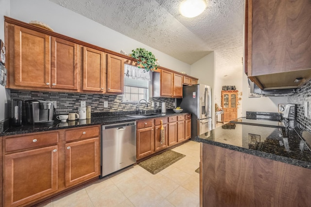 kitchen featuring decorative backsplash, stainless steel appliances, dark stone counters, sink, and a textured ceiling